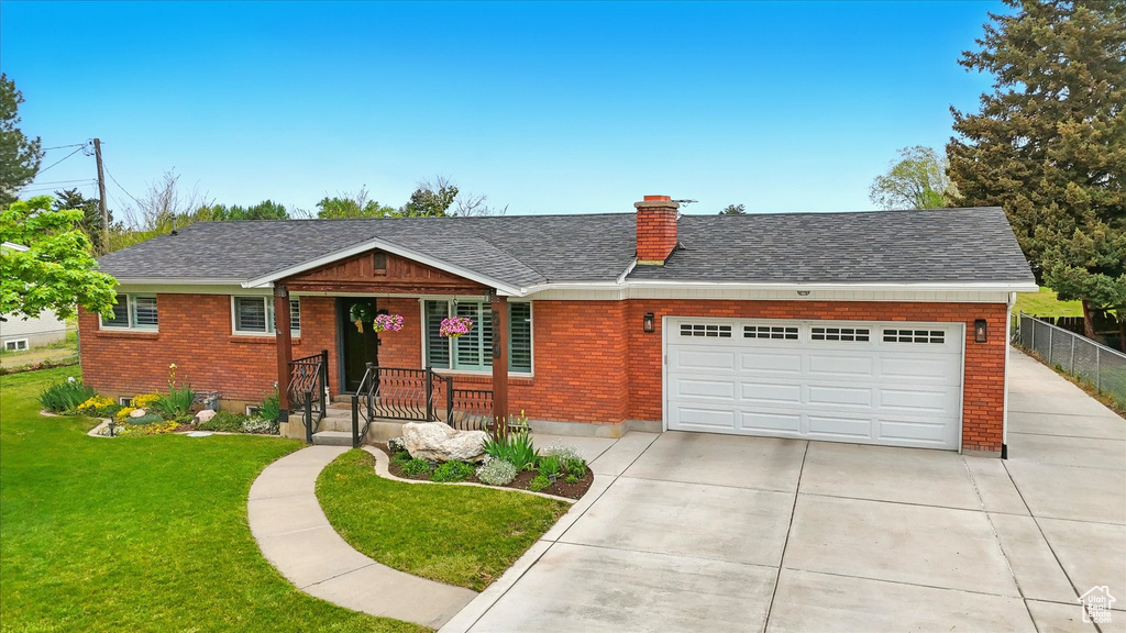Single story home with a chimney, brick siding, an attached garage, concrete driveway, and a front lawn