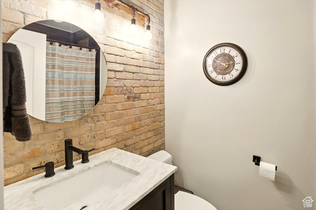 Full bathroom featuring toilet, curtained shower, vanity, and brick wall