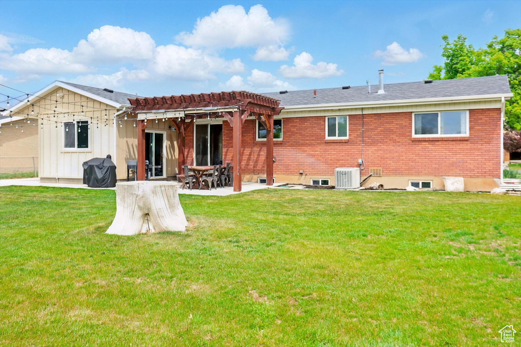 Rear view of property with central air condition unit, a patio area, a pergola, and a lawn