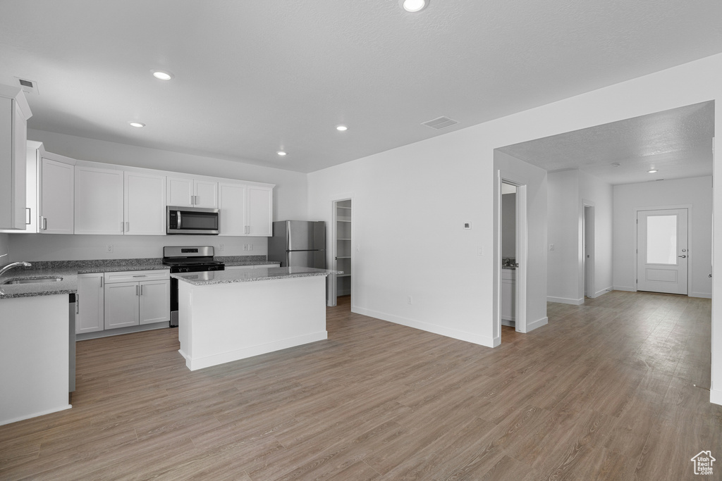Kitchen featuring a sink, open floor plan, a center island, white cabinets, and appliances with stainless steel finishes