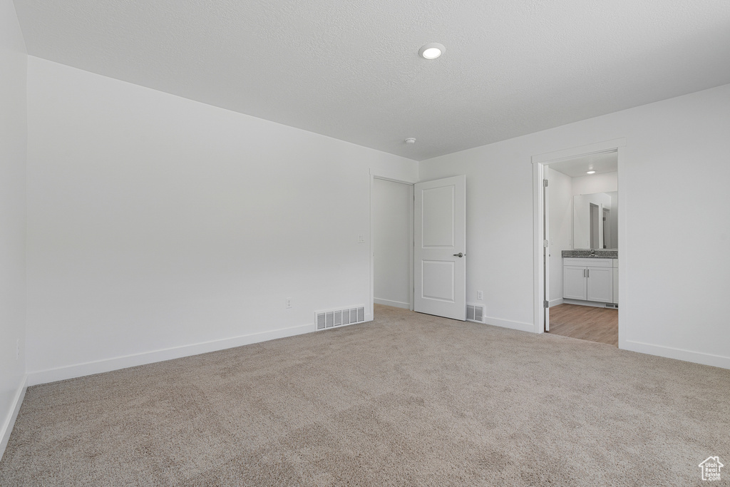 Unfurnished bedroom featuring connected bathroom, visible vents, baseboards, and light carpet