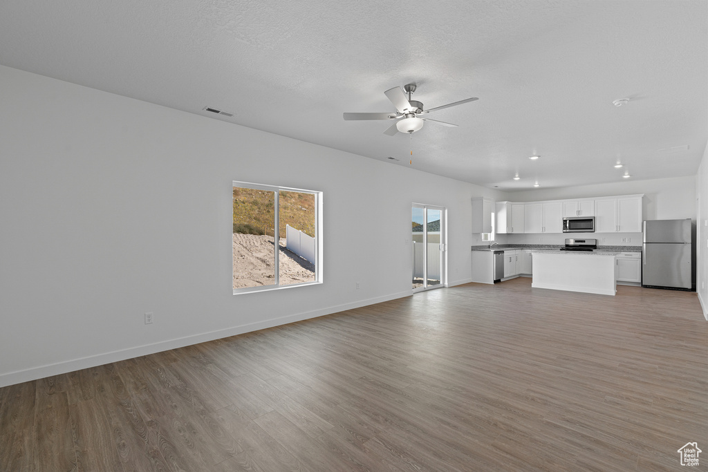 Unfurnished living room with light wood-type flooring, baseboards, visible vents, and ceiling fan