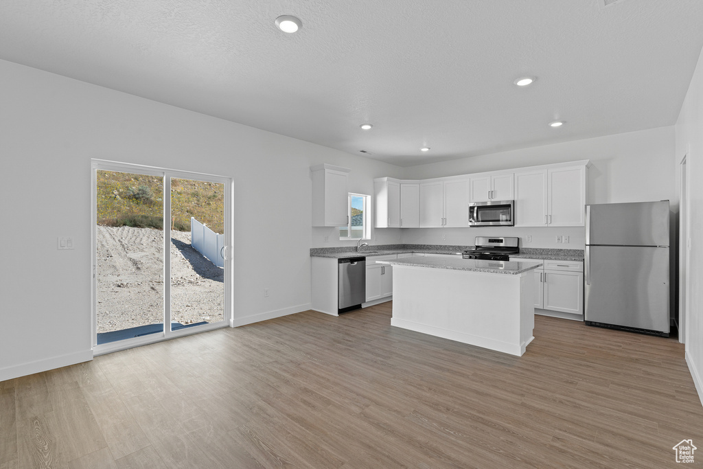 Kitchen with white cabinets, a center island, light wood-type flooring, and appliances with stainless steel finishes