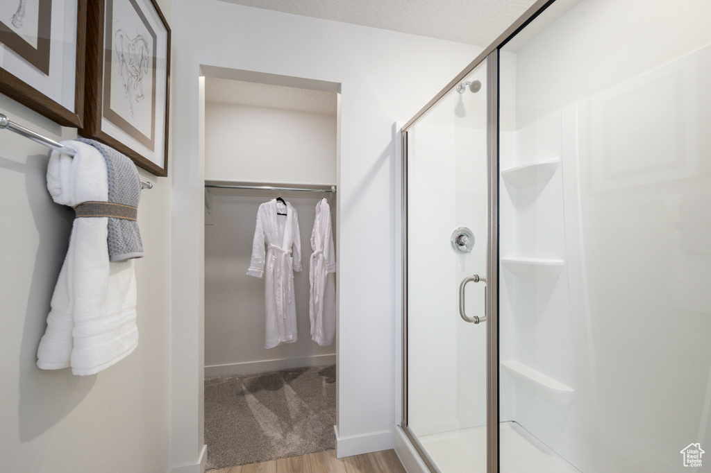 Full bath with a stall shower, a walk in closet, baseboards, and wood finished floors
