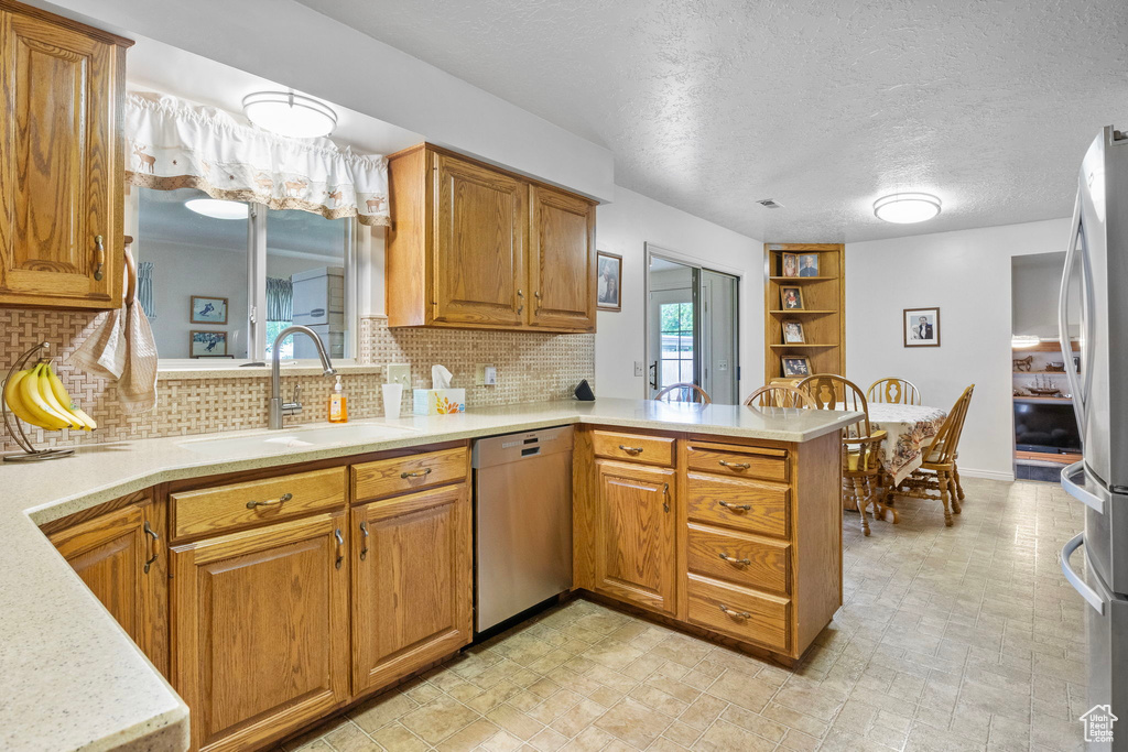 Kitchen featuring a sink, a peninsula, backsplash, light countertops, and appliances with stainless steel finishes