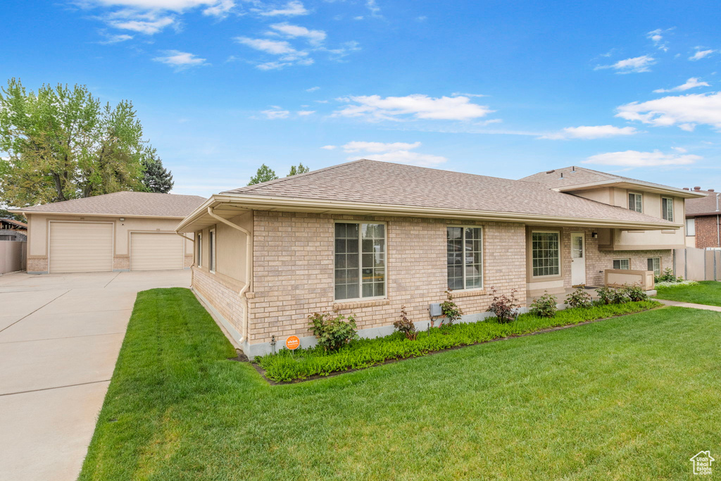 Split level home with a front lawn, a shingled roof, fence, and a detached garage