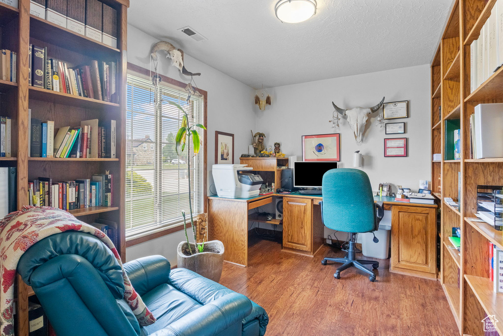 Office space with light wood-style floors, visible vents, and a textured ceiling