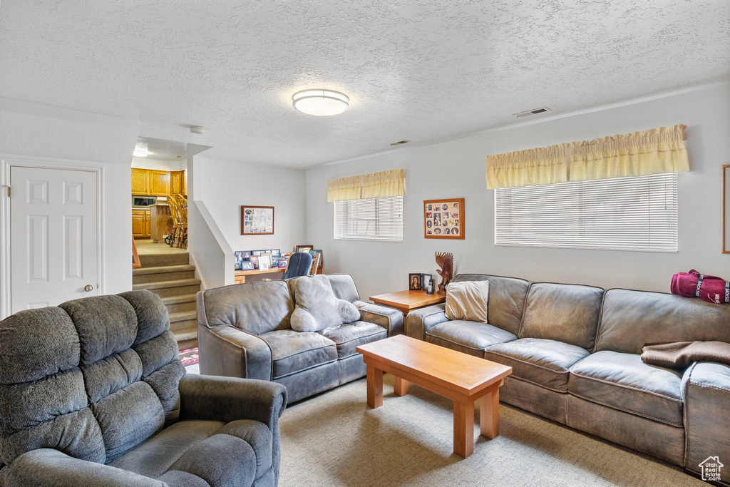 Carpeted living room featuring a textured ceiling, visible vents, and stairway