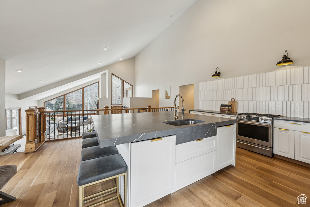 Kitchen featuring a sink, stainless steel gas stove, high vaulted ceiling, white cabinets, and dark countertops