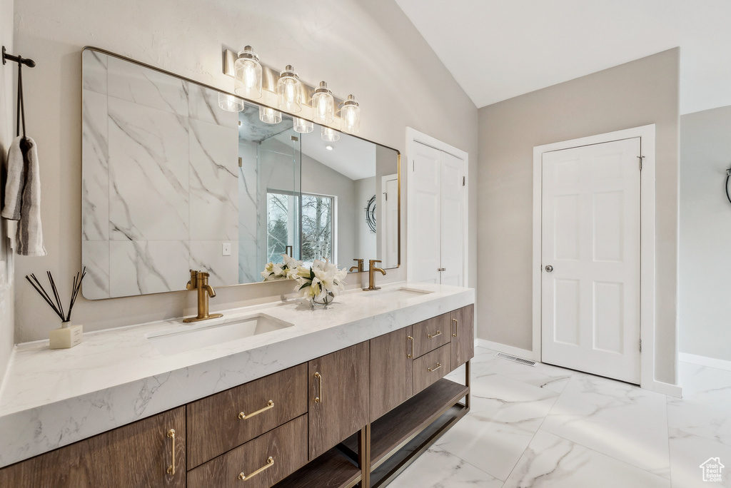 Bathroom featuring double vanity, marble finish floor, lofted ceiling, and a sink