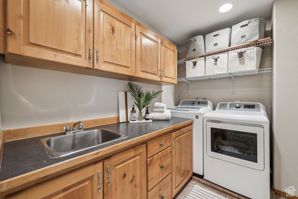 Laundry area featuring washing machine and dryer, light tile patterned flooring, a sink, and cabinet space