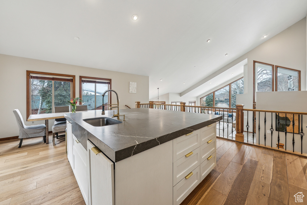 Kitchen with light wood finished floors, a sink, a kitchen island with sink, dark countertops, and white cabinets