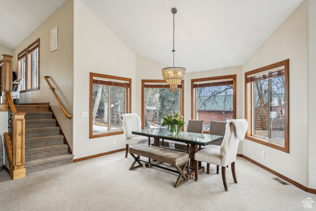 Dining area with lofted ceiling, light colored carpet, visible vents, a chandelier, and baseboards