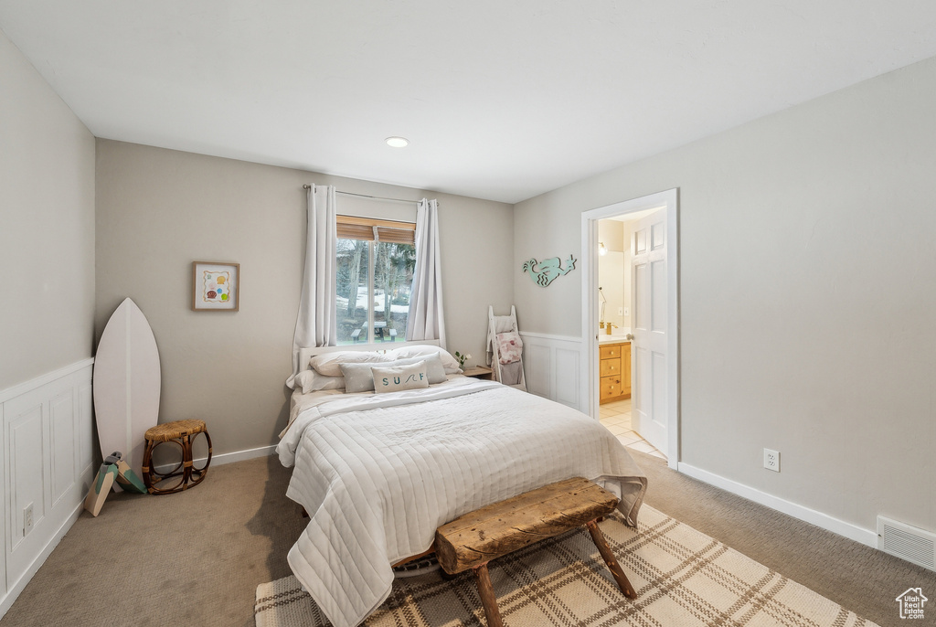 Bedroom with wainscoting, light colored carpet, ensuite bathroom, and visible vents