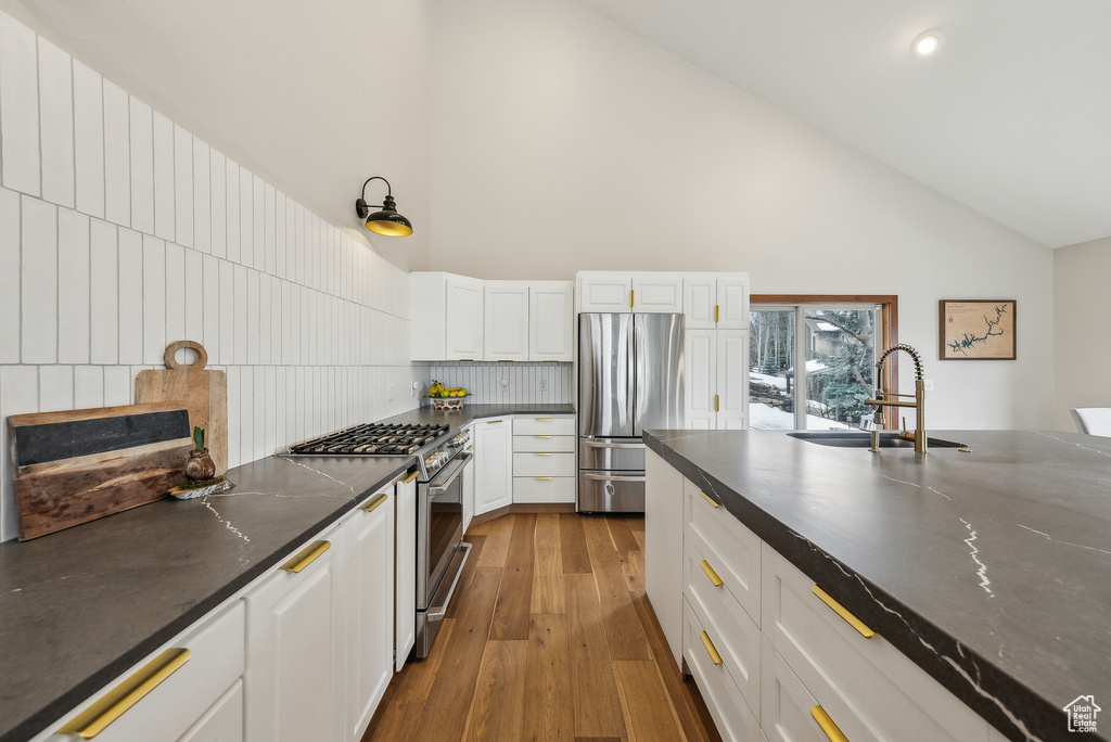 Kitchen with a sink, stainless steel appliances, wood finished floors, high vaulted ceiling, and white cabinetry
