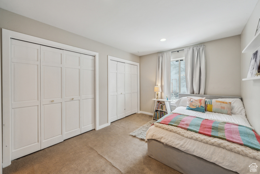 Bedroom with light colored carpet, baseboards, multiple closets, and recessed lighting