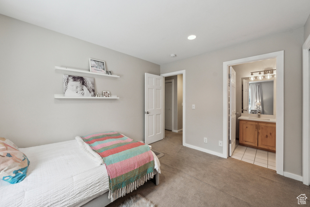Bedroom featuring a sink, ensuite bathroom, light colored carpet, light tile patterned flooring, and baseboards