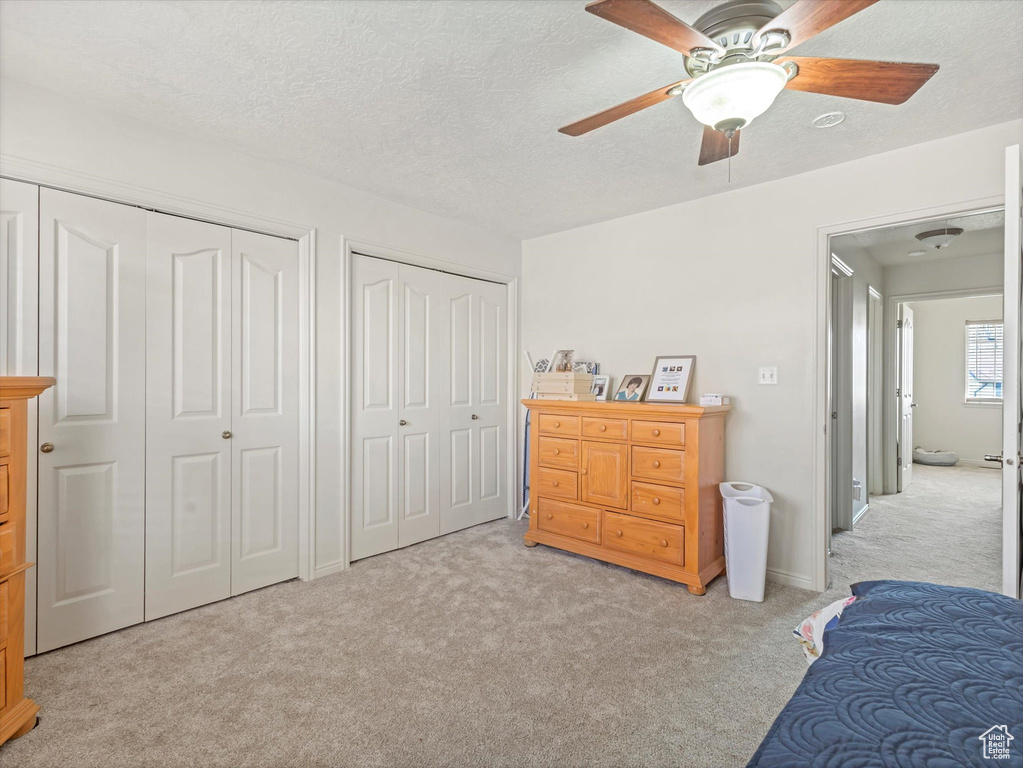 Bedroom with light colored carpet, a textured ceiling, a ceiling fan, and multiple closets