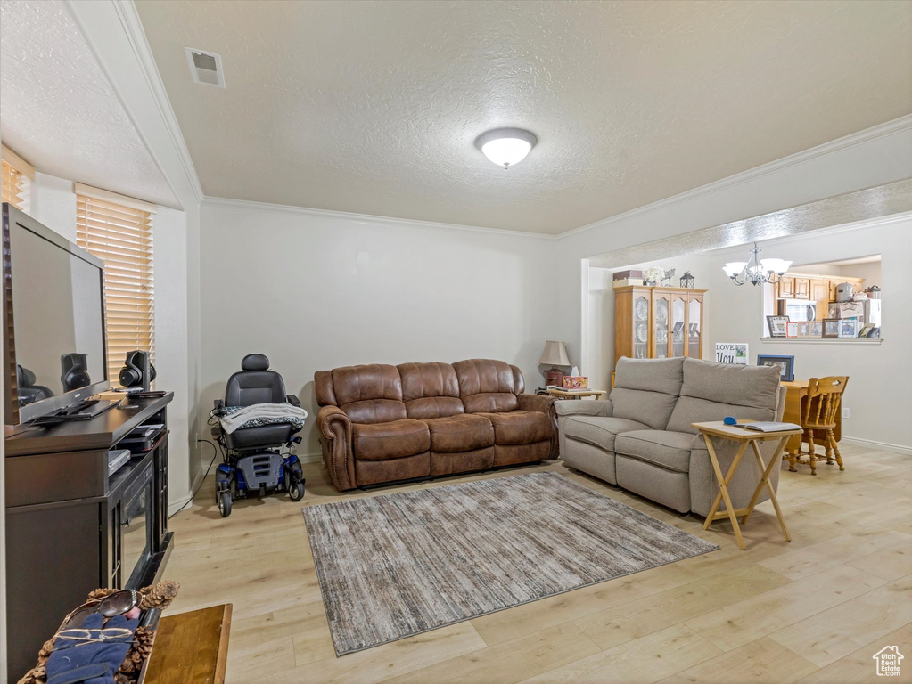 Living room with ornamental molding, visible vents, an inviting chandelier, and light wood-type flooring