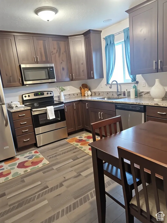 Kitchen with appliances with stainless steel finishes, a sink, dark brown cabinets, and light stone countertops