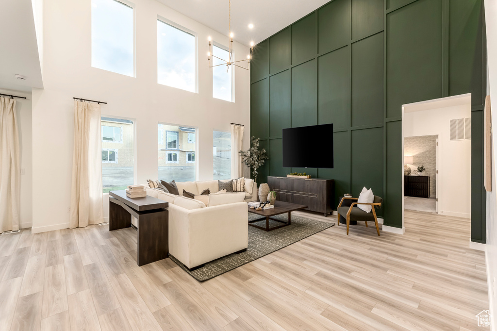 Living room with light wood-style flooring, a high ceiling, a notable chandelier, and a wealth of natural light