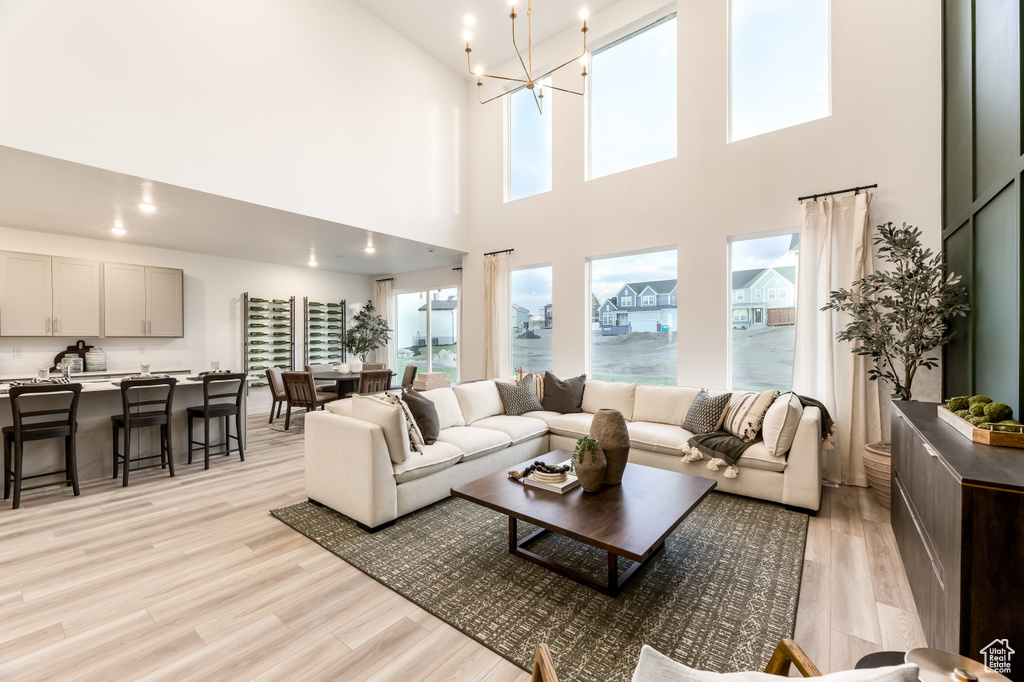 Living room with light wood-style floors, a towering ceiling, and a notable chandelier
