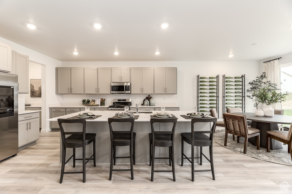 Kitchen with a breakfast bar area, gray cabinets, light countertops, appliances with stainless steel finishes, and recessed lighting