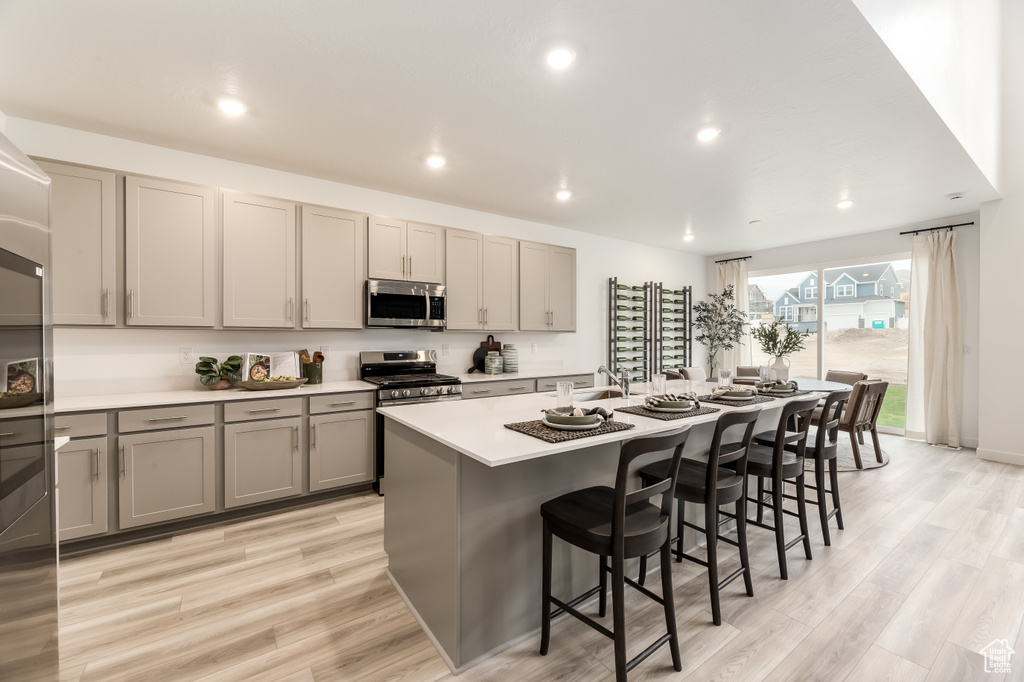 Kitchen featuring stainless steel appliances, gray cabinetry, a breakfast bar, light countertops, and a kitchen island with sink