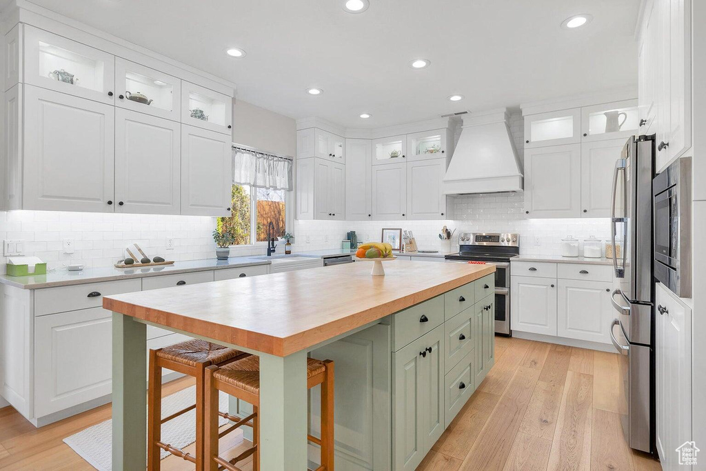 Kitchen with custom exhaust hood, butcher block counters, white cabinets, and appliances with stainless steel finishes