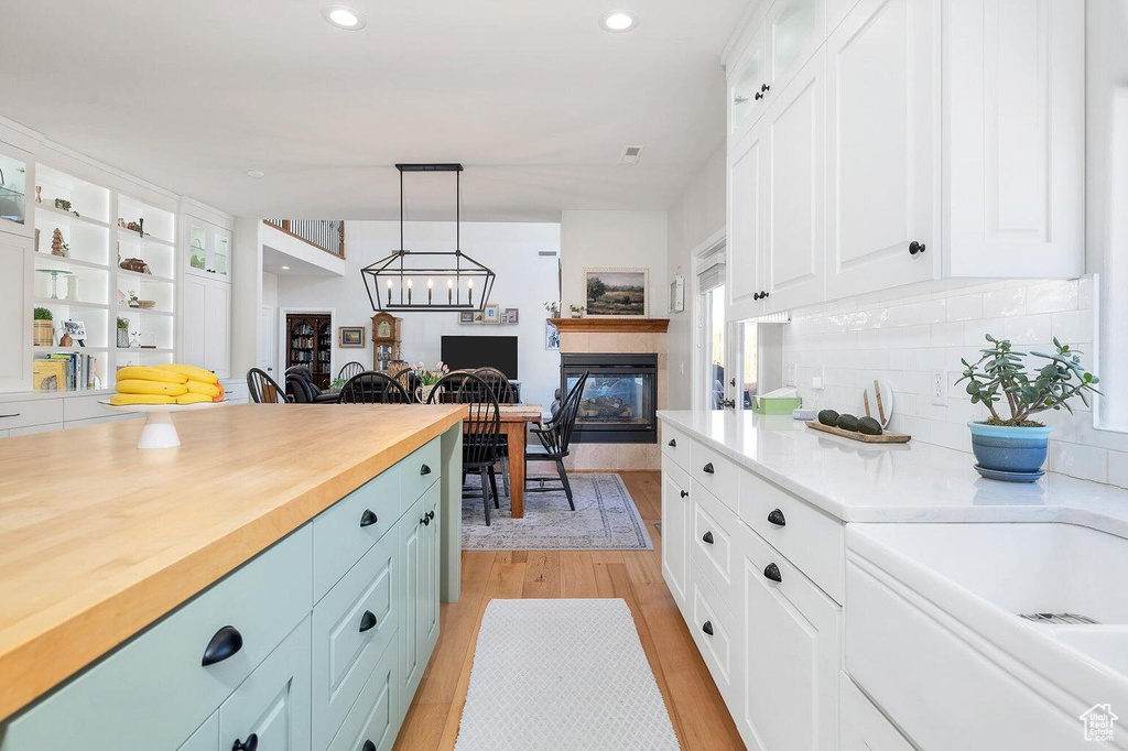 Kitchen with glass insert cabinets, light wood-style flooring, white cabinets, decorative light fixtures, and decorative backsplash