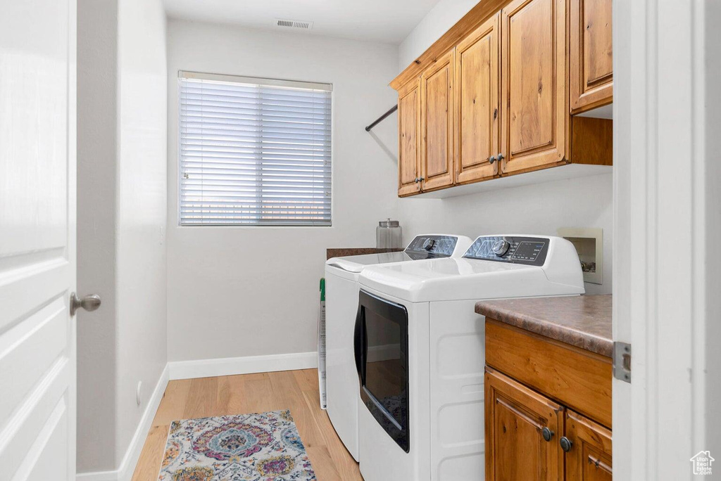 Clothes washing area with cabinet space, washing machine and clothes dryer, light wood-type flooring, visible vents, and baseboards