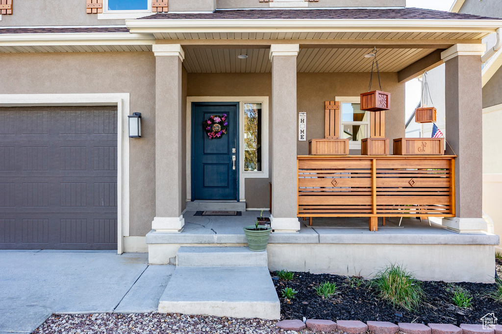View of exterior entry featuring stucco siding, roof with shingles, covered porch, and a garage