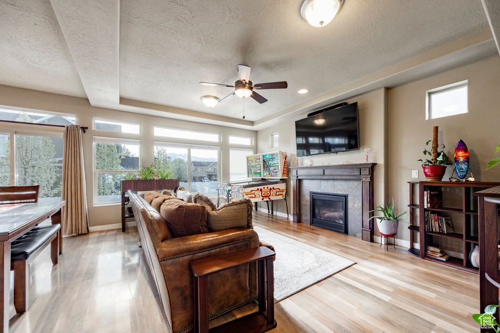 Living area featuring a textured ceiling, a fireplace, a ceiling fan, and a raised ceiling