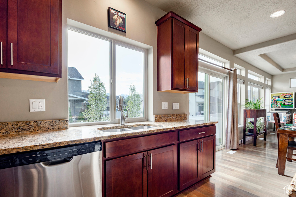 Kitchen featuring light stone countertops, a sink, light wood-type flooring, and stainless steel dishwasher