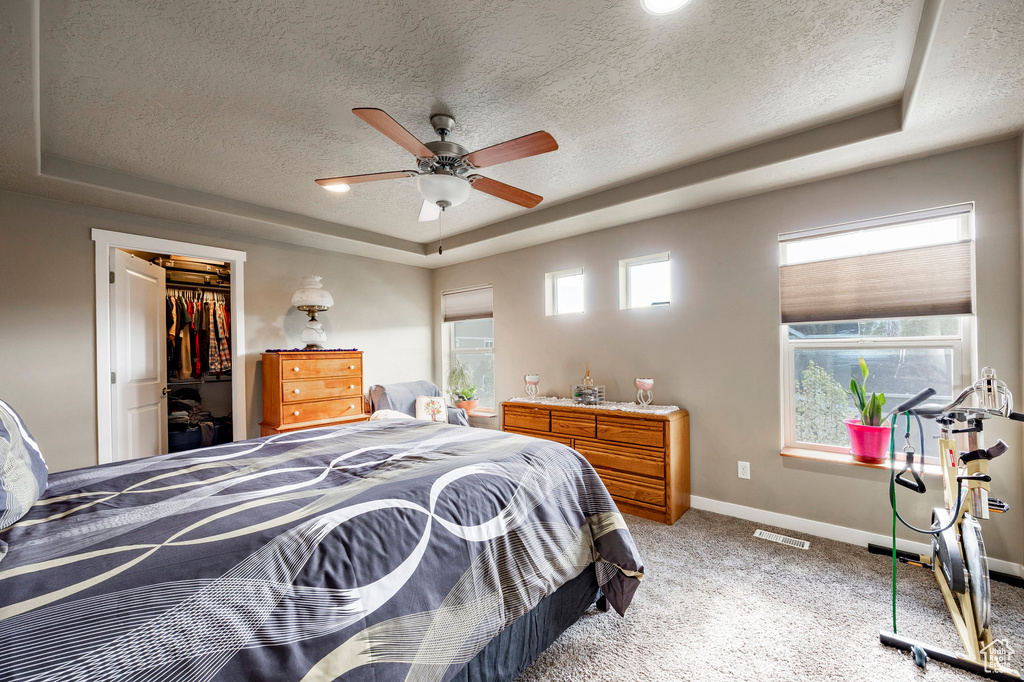 Bedroom featuring light colored carpet, a textured ceiling, a ceiling fan, a tray ceiling, and baseboards