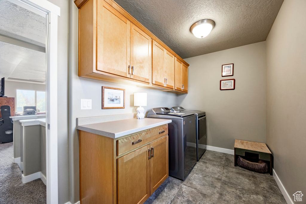 Washroom featuring separate washer and dryer, a textured ceiling, cabinet space, and baseboards