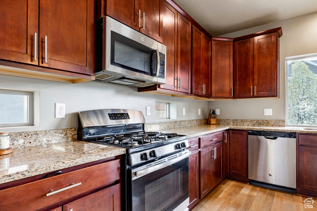 Kitchen featuring light wood finished floors, stainless steel appliances, and light stone countertops
