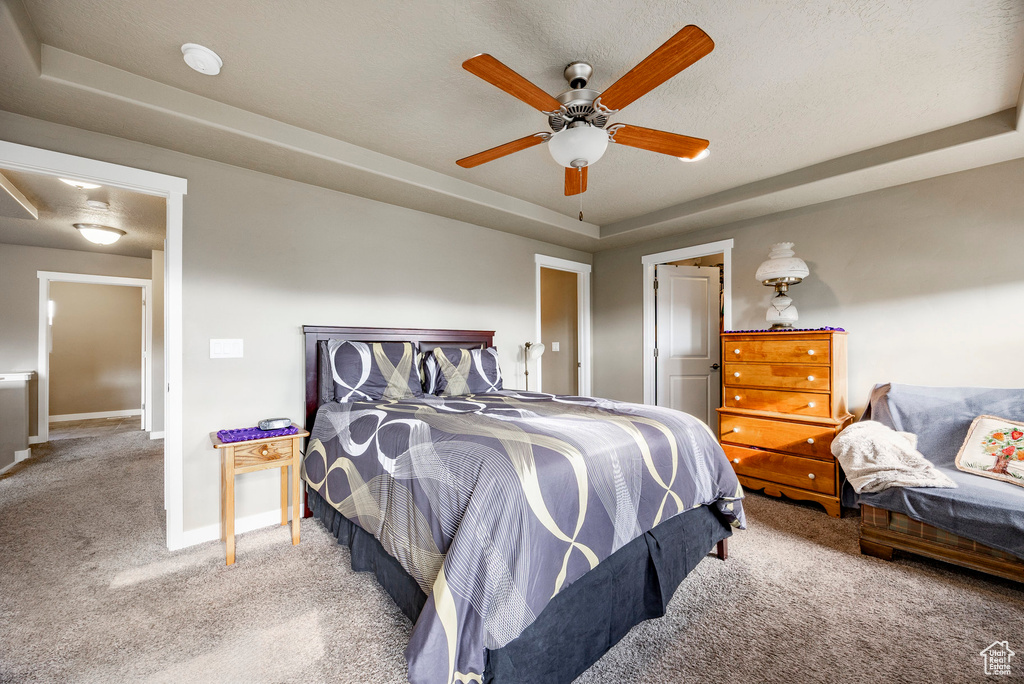 Carpeted bedroom with a ceiling fan, baseboards, and a raised ceiling