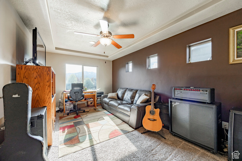 Living room with a desk, ceiling fan, a raised ceiling, plenty of natural light, and a textured ceiling