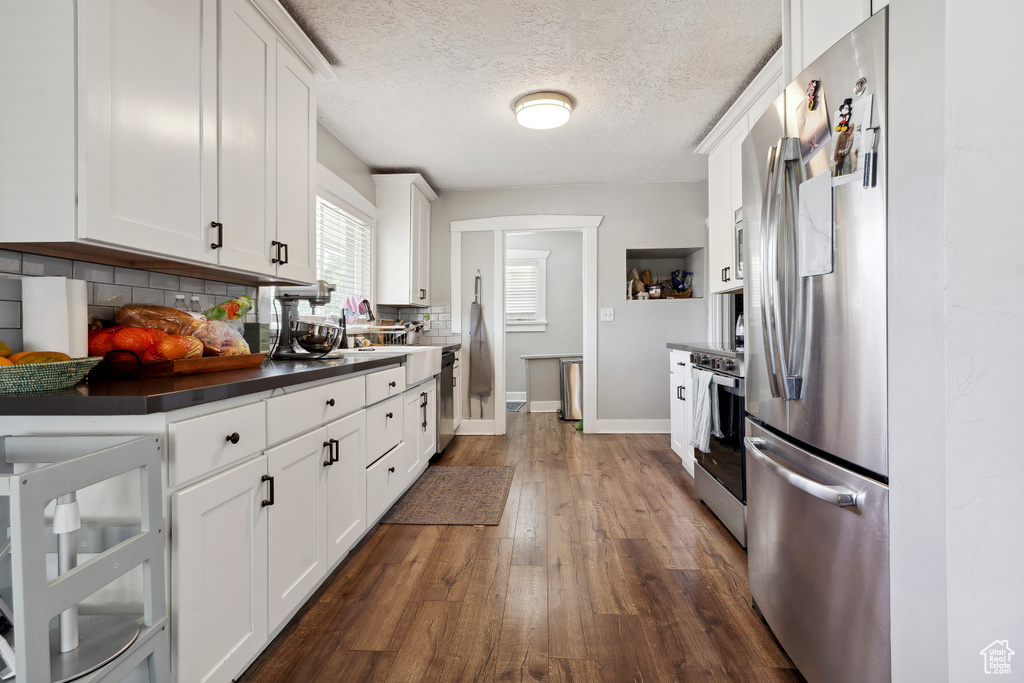 Kitchen featuring dark countertops, dark wood finished floors, white cabinetry, appliances with stainless steel finishes, and decorative backsplash