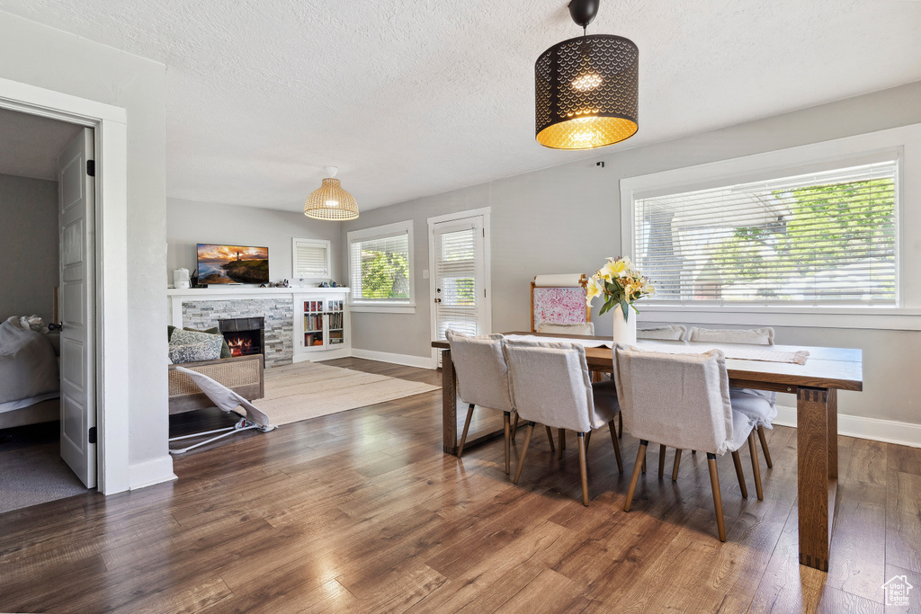 Dining space featuring baseboards, a stone fireplace, a textured ceiling, and wood finished floors