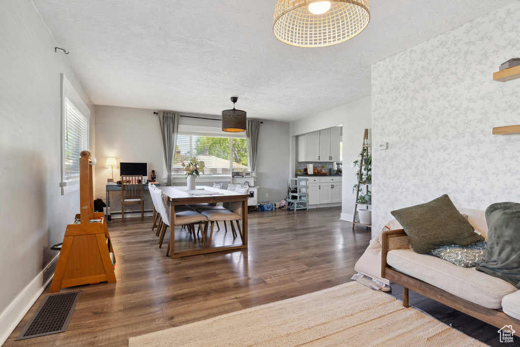 Living room with wood finished floors, wallpapered walls, a textured ceiling, visible vents, and baseboards