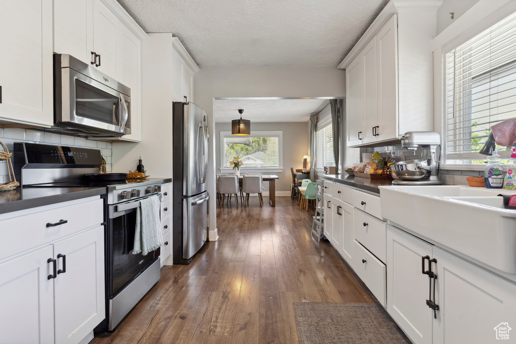 Kitchen with white cabinets, dark countertops, appliances with stainless steel finishes, and tasteful backsplash