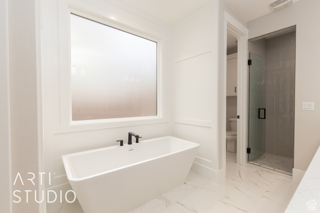 Full bath with toilet, a shower stall, a freestanding tub, marble look tile flooring, and baseboards