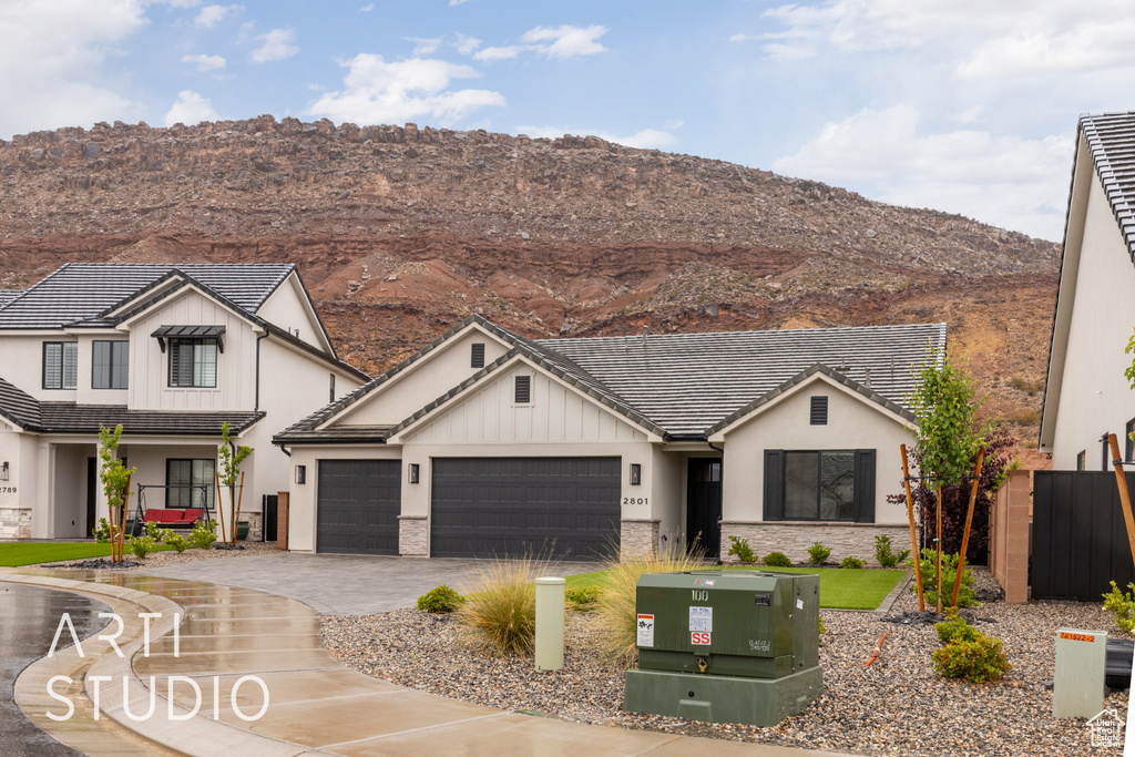 Modern farmhouse featuring an attached garage, a mountain view, decorative driveway, and stucco siding