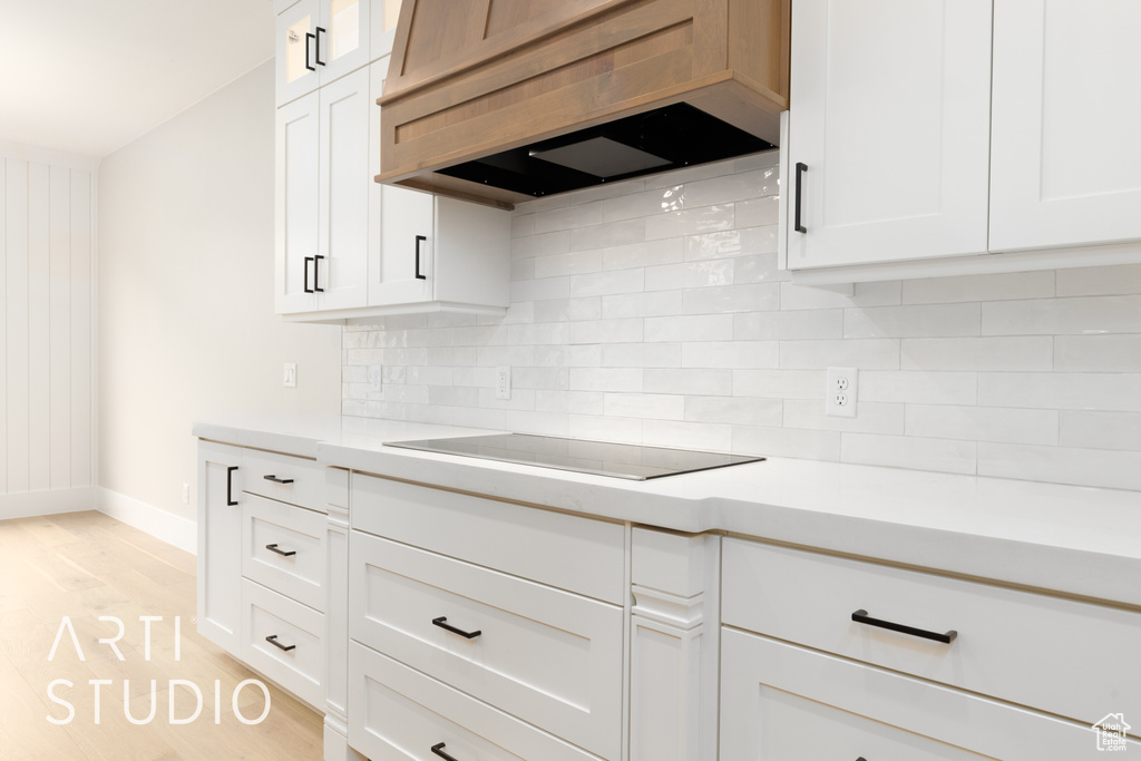 Kitchen with premium range hood, black electric cooktop, light countertops, and baseboards