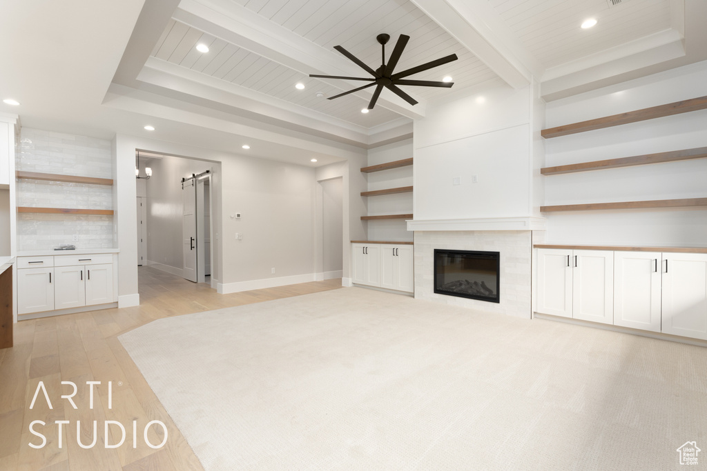 Unfurnished living room featuring a barn door, a ceiling fan, light wood-type flooring, recessed lighting, and beamed ceiling