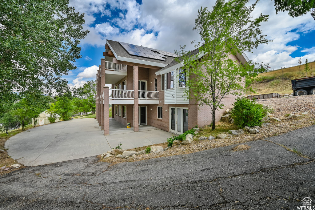 View of front of house with a balcony, a patio, and roof mounted solar panels