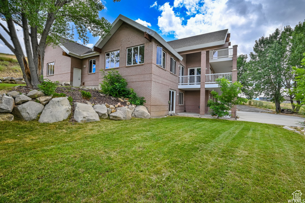 Rear view of house with brick siding, a lawn, and a balcony