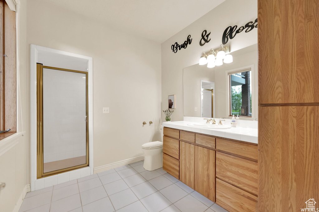Bathroom featuring toilet, a stall shower, baseboards, tile patterned flooring, and vanity